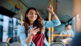 Mujer joven, viendo su celular con una sonrisa, mientras viaja en un autobús. 